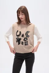 Chaleco de punto sin mangas en color beige con efecto confetti y diseño de jacquard frontal en color negro con motivos de herradura, luna y pájaro. Cuenta con cuello redondo y acabados acanalados.