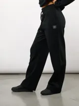 Pantalón de corte recto confeccionado en felpa, con cintura elástica ajustable mediante cordón y bolsillos laterales. Presenta un diseño minimalista con el logo de la marca sutilmente bordado en la parte frontal.