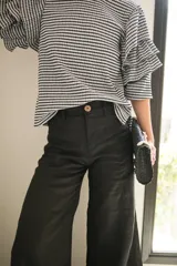 Blusa de tela con estampado vichy en blanco y negro, con cuello redondo y mangas con tres volados escalonados que llegan hasta el codo. Presenta puños elásticos y cierre con botón en la parte posterior.