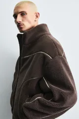 Cazadora de corte relajado confeccionada en tejido de borreguillo con diseño de paneles en tonos marrón y beige. Presenta cuello subido, cierre frontal de cremallera, bolsillos laterales y acabados en rib en puños y cintura.