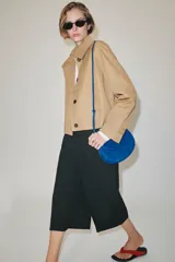 Chaqueta corta de cuello subido y manga larga con trabilla y botón. Cuenta con bolsillos de vivo en el delantero y cierre frontal con botones.