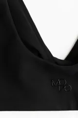 Top deportivo negro para yoga, de tejido funcional con efecto segunda piel y alta elasticidad gracias a la tecnología Lycra® Sport. Diseño con breteles anchos, escote en V profundo y detalle cruzado/girado en el frente. Incluye copas forradas con relleno extraíble.