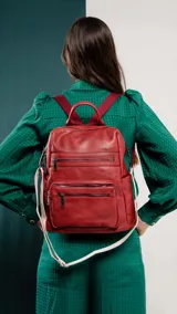 Mochila de símil cuero color marrón con apertura superior y tres bolsillos frontales con cierres metálicos. Cuenta con bolsillos laterales y una correa de galón con diseño geométrico, regulable y extraíble, que permite su uso como bandolera.