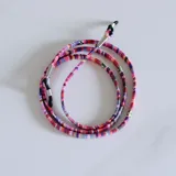 Cuerdita para lentes de tela tejida con patrón multicolor, con terminales metálicos y sujetadores de goma negros en los extremos.