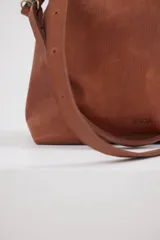 Cartera tipo shopper de cuero color suela, con diseño minimalista, correa larga ajustable y herrajes metálicos en tono bronce.