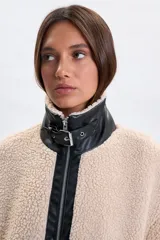 Campera de sherpa color crudo con detalles en cuero sintético negro en el cuello y la solapa frontal. Cuenta con cierre frontal y cuello alto con hebilla ajustable.