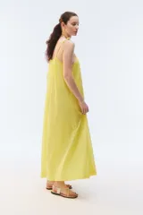 Vestido maxi solero amplio y largo de color amarillo, con escote redondo, frunces que otorgan vuelo, breteles finos ajustables con nudo en los hombros y bolsillos laterales.