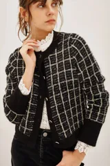 Cardigan de punto en color negro con diseño de cuadros en color beige. Presenta cuello redondo, cierre frontal con botones metálicos y mangas largas con puños anchos en color negro liso.