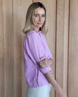 Camisa de manga tres cuartos color beige con cuello con volados y botones frontales. Presenta un detalle de color negro en la parte superior de las mangas.