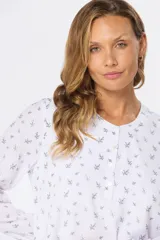 Blusa blanca de manga larga con estampado de pequeñas ramas negras, cuello redondo con abertura y cierre frontal con botones.