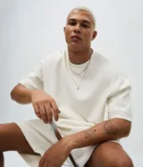 Remera oversize de color blanco hueso, con cuello redondo y mangas cortas de sisa desplazada, confeccionada en mezcla de algodón.