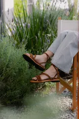 Sandalias bajas de cuero color marrón, con tiras finas para atar alrededor del tobillo.