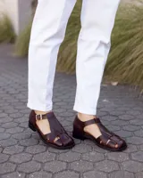 Sandalias estilo romano de cuero marrón oscuro, con diseño de tiras entrelazadas, talón cerrado y hebilla metálica de ajuste lateral.