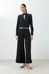 Mono largo negro con textura amasada, cuello mao con abertura en forma de gota, mangas largas y cinturón plateado de eslabones.