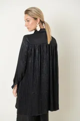 Camisa plateada de poliéster con textura metalizada, corte amplio, cuello clásico, cierre frontal con botones y mangas largas con puños abotonados.