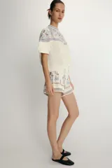 Shorts de tiro alto en color crudo con bordados decorativos en tonos azul y rojo. Presentan un diseño estructurado con cierre lateral oculto.