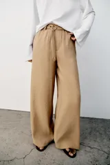 Pantalón recto color beige de tiro medio, con cintura elástica, bolsillos delanteros y cinturón ajustable con hebilla metálica dorada.