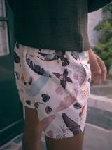 Short de baño blanco con estampado de hojas de palmera, piñas y flores en tonos marrones, rosados, celestes y naranjas.