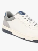 Zapatillas de baloncesto Tommy Hilfiger de corte bajo, color blanco con detalles en gris, azul y suela bitonal. Presentan exterior de piel con paneles de ante y mezcla de texturas, cordones blancos y detalles distintivos de la marca.
