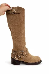 Botas de caña media color marrón claro, confeccionadas en gamuza. Presentan detalles de hebillas y correas metálicas alrededor del tobillo y una hebilla ajustable en la parte superior de la caña. Tienen un tacón bajo y suela gruesa.
