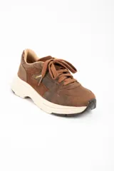 Zapatilla urbana de cuero lavado en tonos marrones, con paneles de gamuza y detalles metalizados en el talón. Presenta cordones al tono y una suela de plataforma de goma en color crema.