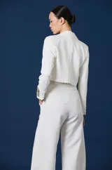 Saco corto tipo blazer color negro, de corte entallado y manga larga. Presenta un detalle distintivo en el puño izquierdo con una banda en tono dorado que incluye la inscripción 'ANTOLIN'.