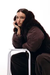 Campera de invierno con frente de piel sintética y capucha integrada, combinada con mangas acolchadas de estilo puffer en color marrón oscuro.