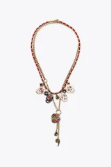 Pack de dos collares. El primero es una cadena doble con abalorios rojos y eslabones dorados, adornado con varios dijes de calaveras esmaltadas con detalles coloridos y piedras oscuras. El segundo collar es una cadena dorada más larga con un dije colgante de corazón esmaltado con motivos florales y un dije en forma de signo de interrogación.