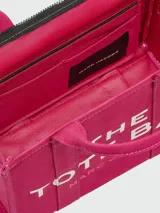 Cartera tipo tote bag de Marc Jacobs, confeccionada en lona color beige con el logo estampado en blanco al frente. Cuenta con doble asa superior, correa de hombro ajustable y extraíble, y cierre superior con cremallera.