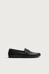 Mocasines de piel color negro, con punta redonda, suela ultrafina y detalle de tira con hebilla metálica dorada en el empeine.