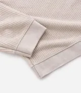 Polo de manga larga color beige claro, confeccionado en tejido texturizado (posiblemente acanalado o waffle). Presenta un cuello polo con escote profundo en V sin botones.