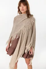 Ruana de punto color beige con diseño abierto y flecos en los bordes.