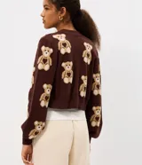 Cardigan corto de punto jacquard color marrón, con estampado de ositos en repetición, cuello en V, mangas largas y cierre frontal con botones.