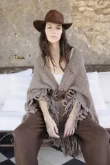 Ruana tejida a mano en lana merino, con diseño amplio, textura de punto y terminaciones con flecos largos en los bordes.