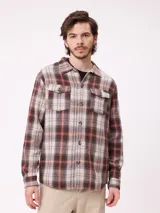 Camisa de franela gruesa con diseño a cuadros en tonos marrones, beige y azul. Presenta cuello clásico, cierre frontal con botones y dos bolsillos en el pecho con solapa y botón.