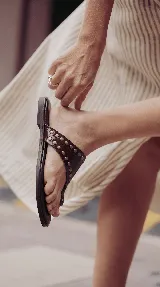 Sandalias chatas de cuero color bordó, con diseño de tira ancha que envuelve el empeine y sujeta el dedo gordo, decoradas con tachas metálicas doradas.