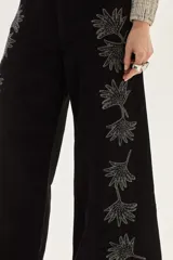 Jean de corte pata ancha color negro, con diseño de paneles frontales y bordados florales a lo largo de las piernas.