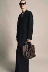 Bolso tipo saca de piel color marrón oscuro, con cuerpo fruncido y doble asa de mano rígida metálica. Incluye asa extraíble para llevar al hombro o cruzado y bolsillo interior extraíble.