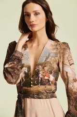 Vestido largo Natalia Antolin modelo Serenna, con escote en V profundo, mangas largas, faja en la cintura y falda larga con vuelo. Presenta un estampado artístico estilo pintura clásica con caballos y paisajes naturales en tonos marrones y beige.