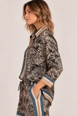 Camisa de satén con estampado animal print tipo cebra en tonos camel y negro, con cuello camisero, botonadura frontal y puños anchos con ribetes.