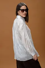 Camisa blanca de corte holgado, con cuello clásico y cierre frontal de botones. Presenta un delicado bordado de mariposas en toda la prenda y mangas largas con puños abotonados.