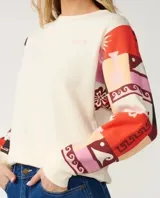 Buzo de cuello redondo color off white, con mangas largas estampadas con diseño patchwork multicolor en tonos rojos, rosas y negros.