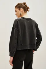 Buzo de algodón color negro con efecto lavado, corte holgado y detalles de tachas metálicas plateadas alrededor del cuello redondo y en los hombros.