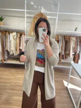 Saco largo color crema, de tejido de punto, con bolsillos laterales y corte recto.