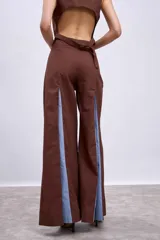 Pantalón largo color marrón, de corte ancho y tiro alto, con aberturas frontales en las piernas que revelan paneles internos en tono celeste.