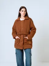 Campera de pana color marrón, con diseño acolchado, cuello camisero, cierre frontal oculto y cinturón ajustable con hebilla a tono. Presenta bolsillos frontales con solapa y mangas largas de corte holgado.