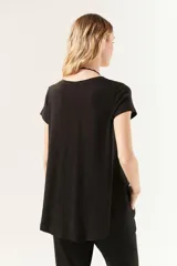 Remera negra de manga corta con cuello redondo y corte amplio, con ruedo asimétrico y más largo en la espalda.