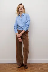 Camisa blanca de manga larga con cuello clásico y botones frontales. Tiene un bolsillo en el pecho con un pequeño logo bordado.