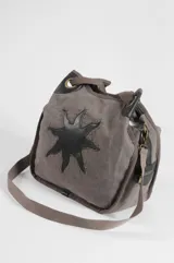 Bolso oversize negro de canvas con diseño de sol en eco-cuero marrón aplicado en el frente, bordeado con tachas metálicas. Cuenta con asas de hombro y detalles de herrajes en tono bronce.