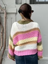 Buzo de tejido de punto grueso con diseño de rayas horizontales multicolores en tonos blanco, rosa, verde oliva y beige. Presenta cuello redondo acanalado, mangas largas con puños ajustados y un corte holgado.